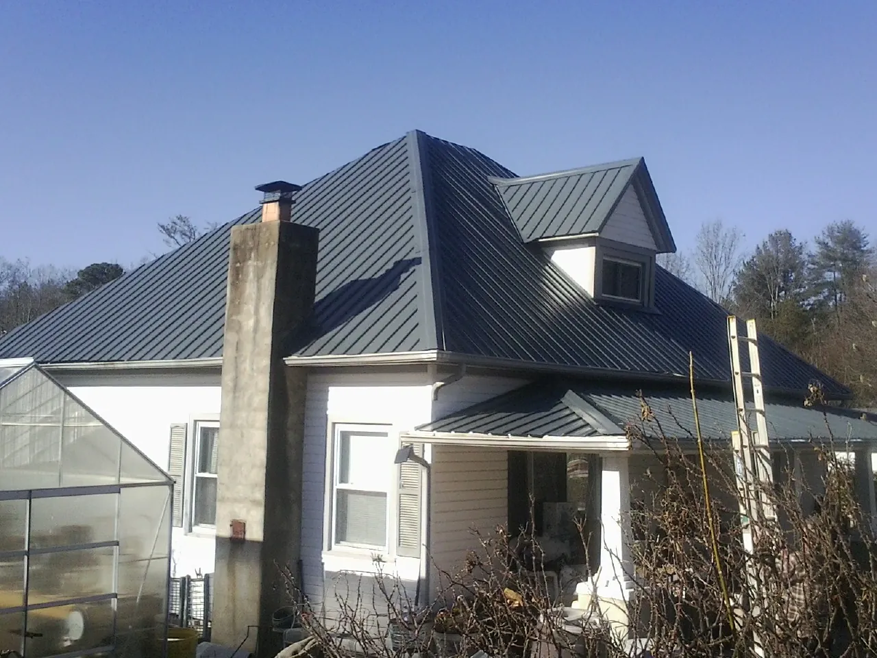 Dark blue standing seam metal roof on a white farmhouse with dormer — Slate & Tile Roof Repair by Roofing Brothers in Elyria