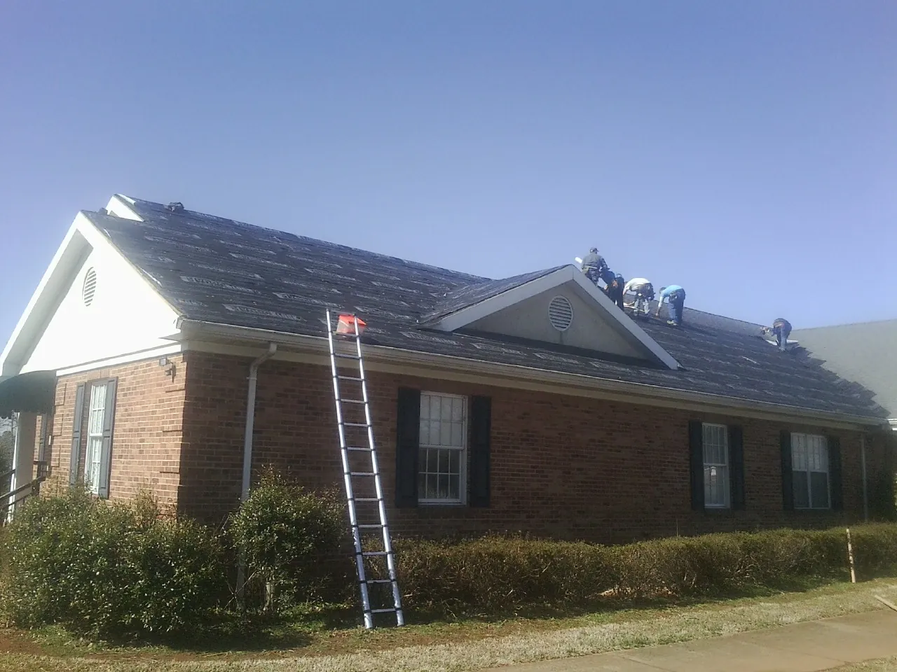 Crew tearing shingles off a brick ranch roof with a ladder set — Emergency Roof Repair work by our crew in Elyria
