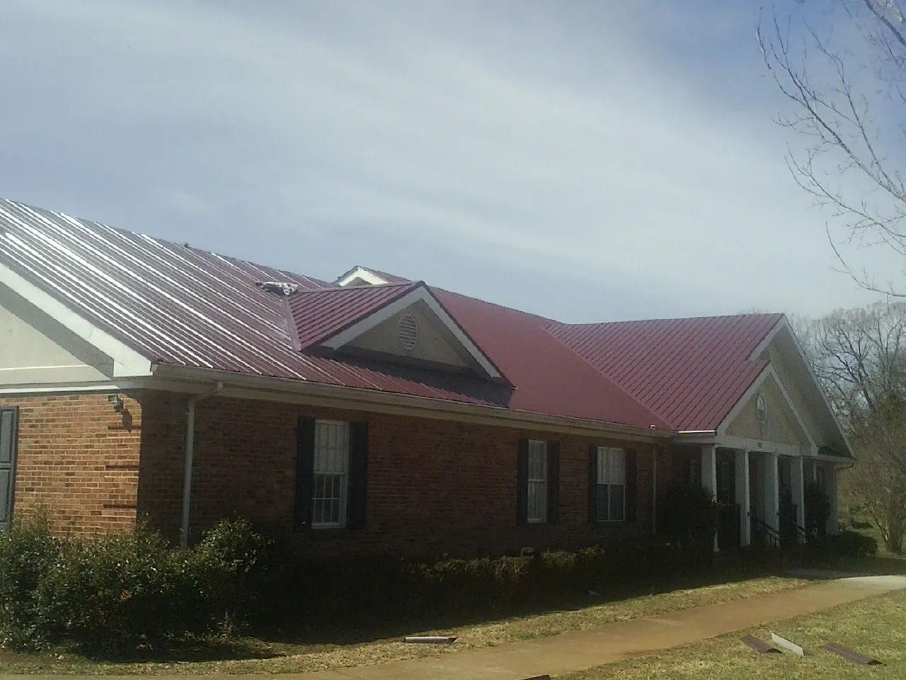 Red metal roof with gabled entries on a long brick building, from a Hail Damage Roof Repair job in Elyria