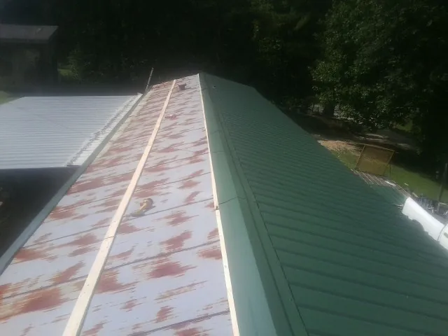 Old rusted panels beside newly installed green metal roofing — Wind Damage Roof Repair by Roofing Brothers in Elyria