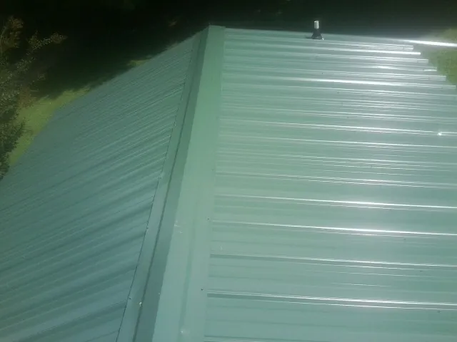 New green metal panels meeting at the ridge of a roof — Flat Roof Repair work by our crew in Elyria