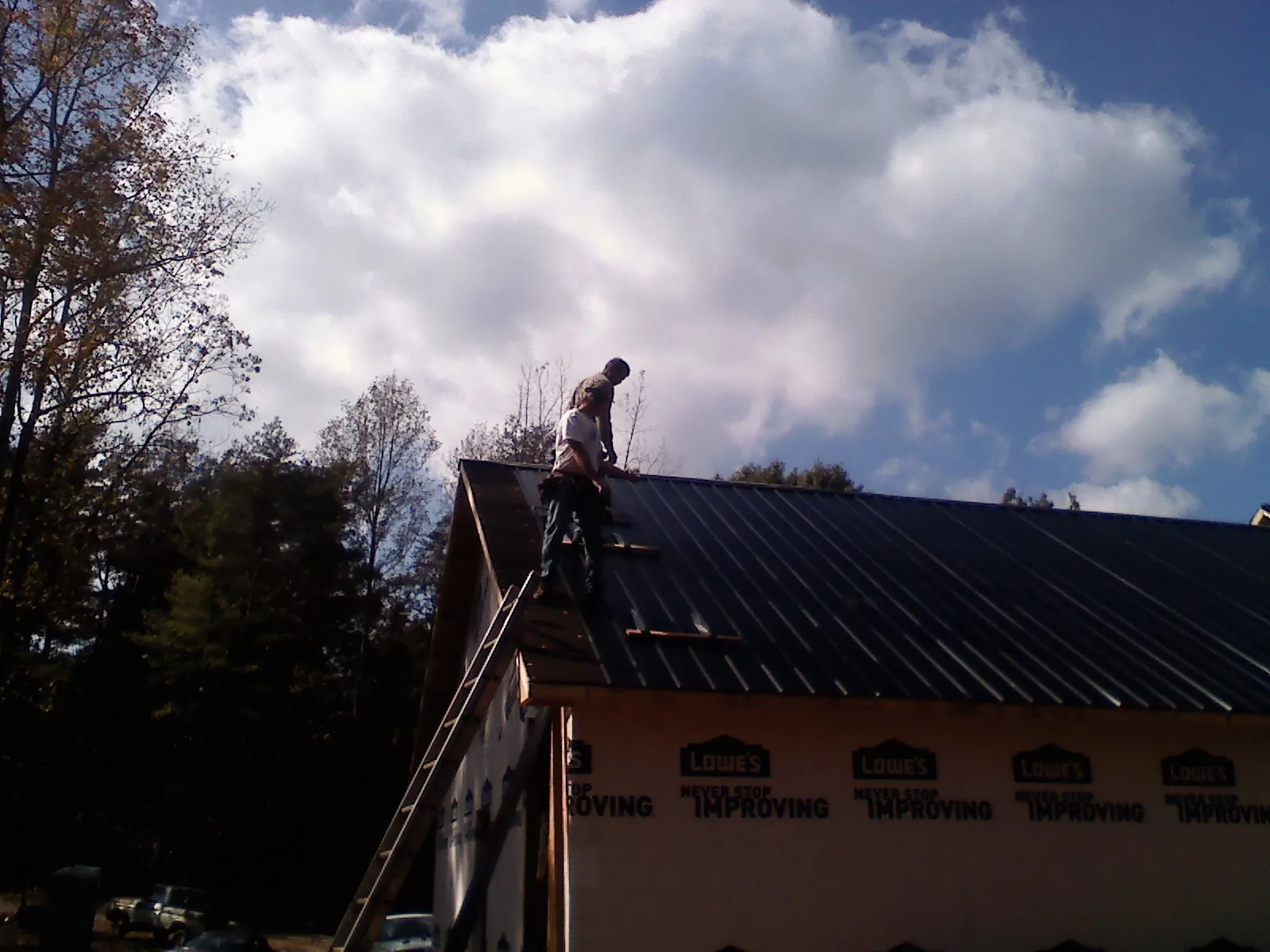 Roofer fastening dark metal panels high against a cloudy sky, from a Roof Inspection job in Elyria